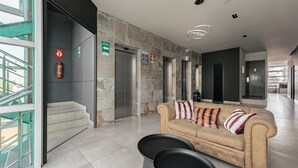Eine moderne Lobby mit einem beigen Sofa, einer Treppe und einem Aufzug.