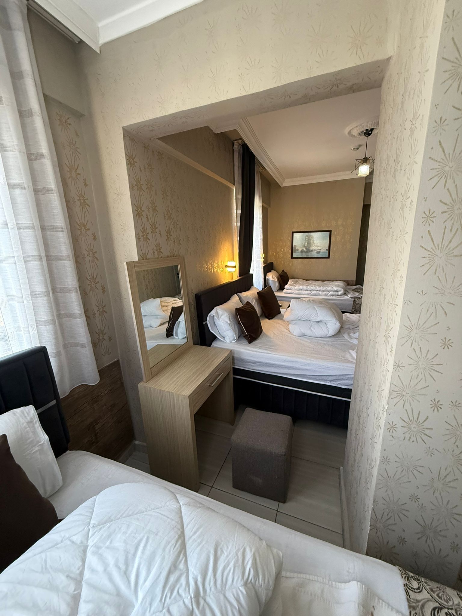 A hotel room with a bed, a desk, a chair, a mirror, and a bedside table.