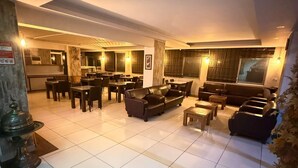 A hotel lobby with a dining area, sofas, and a tiled floor. - Özgür Family Otel (Antalya)