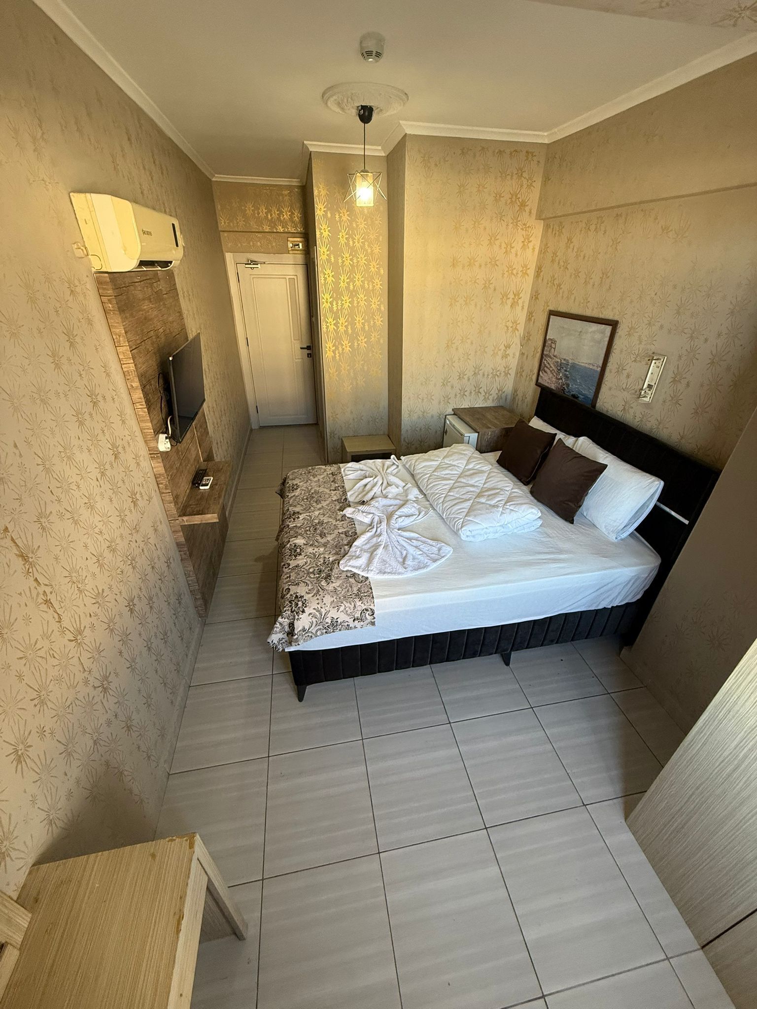 Habitación de hotel con cama, televisión, una mesita y un calentador fijado a la pared.