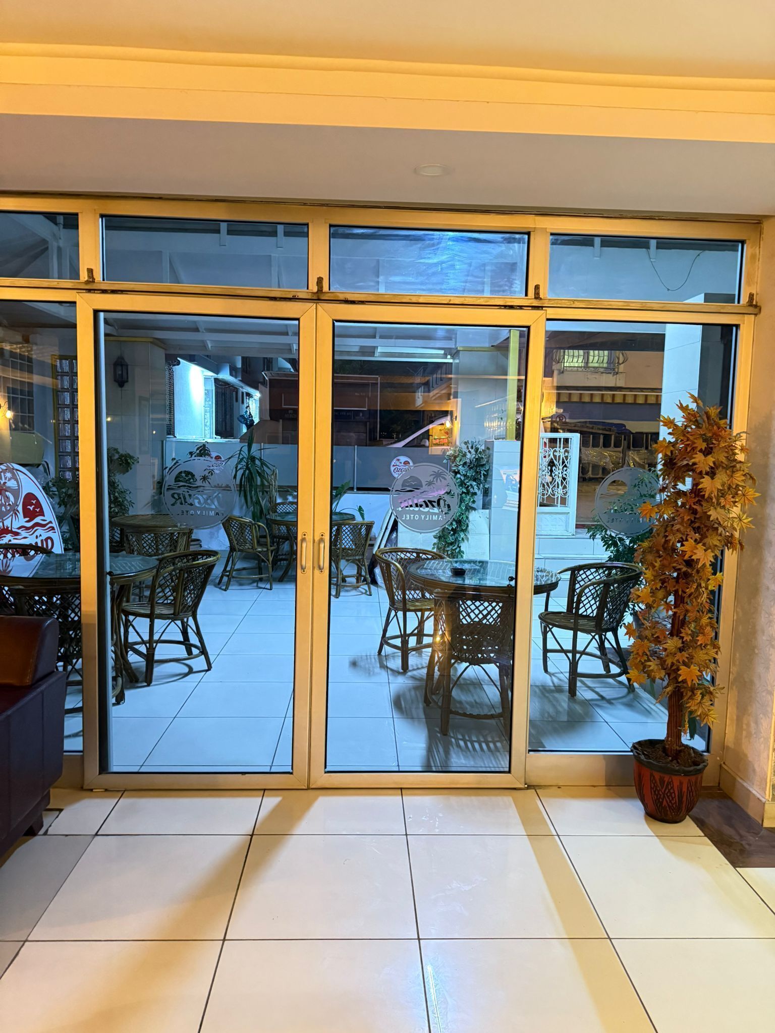 A restaurant with glass doors, wicker furniture, and a potted plant.