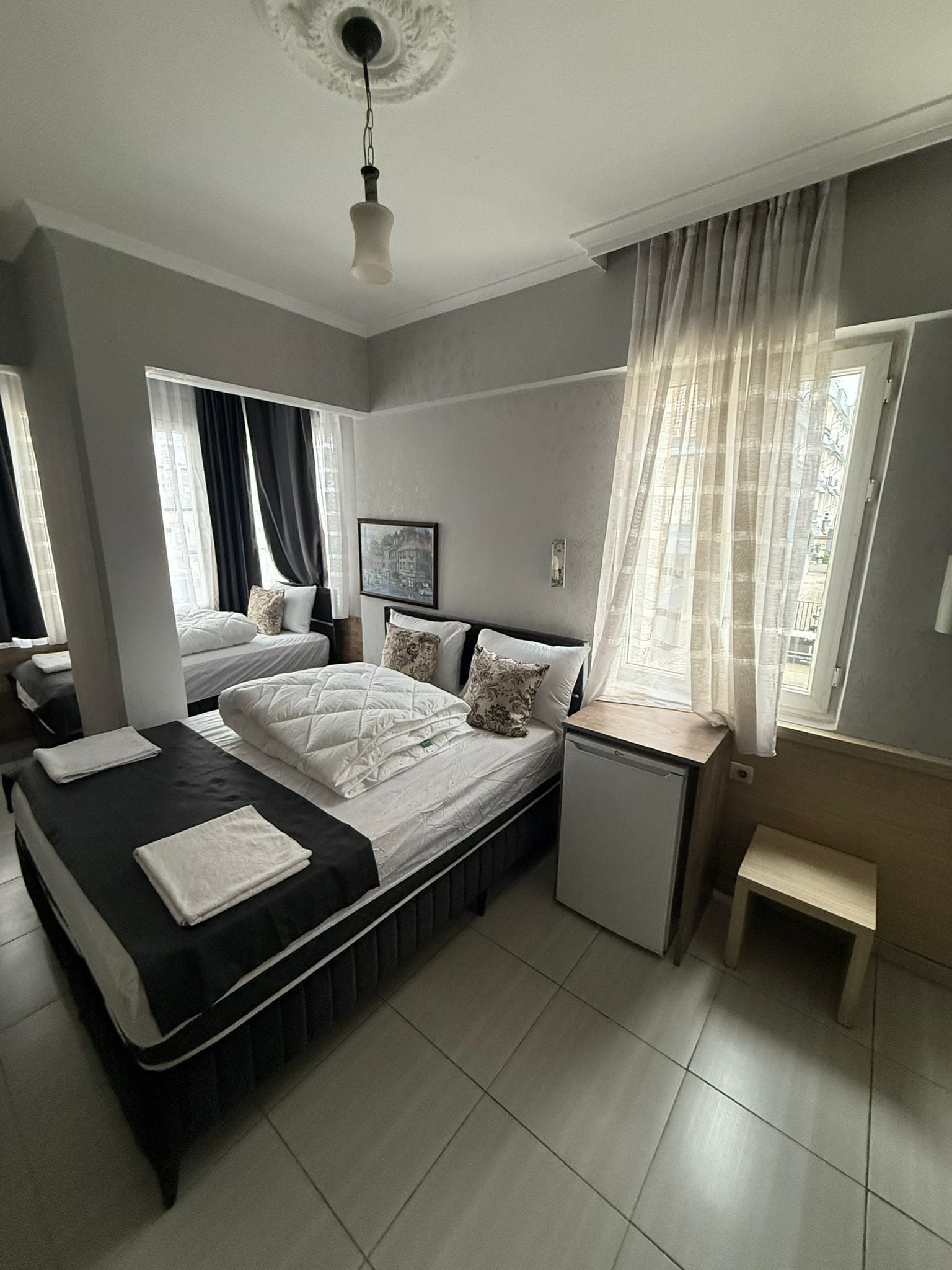 A modern bedroom with a large bed, bedside tables, a small desk, and a window with curtains.