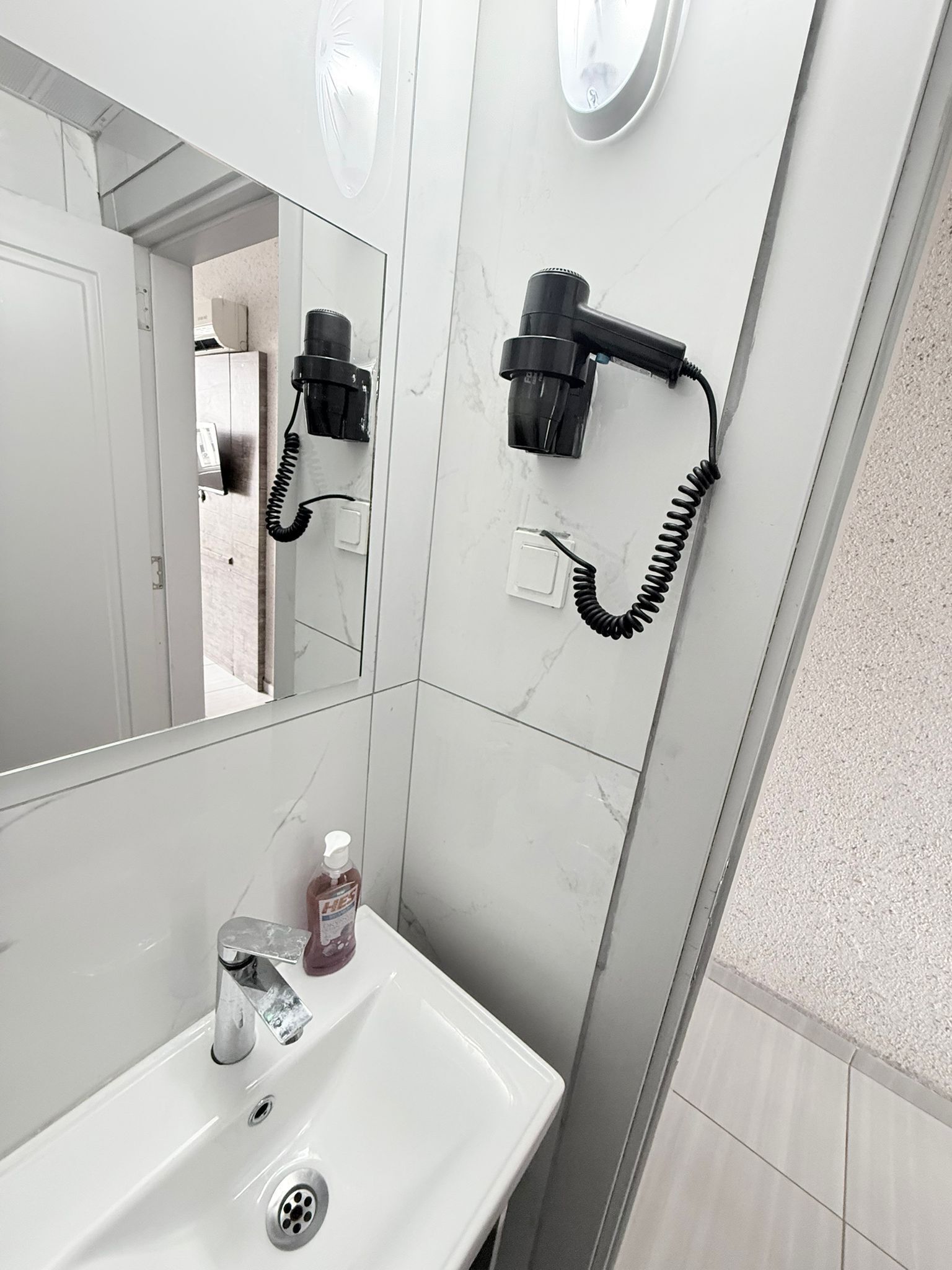 Ein Badezimmer mit einem weißen Waschbecken, einem Spiegel, einem Fön und einer Handseifenflasche.