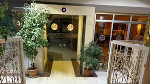 The entrance to Ozgur Family Hotel with a red mat, potted plants, and a tiled floor. - Özgür Family Otel (Antalya)