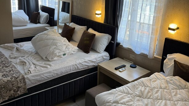 A hotel room with two beds, a bedside table with a remote control, and a mirror. - Özgür Family Otel (Antalya)