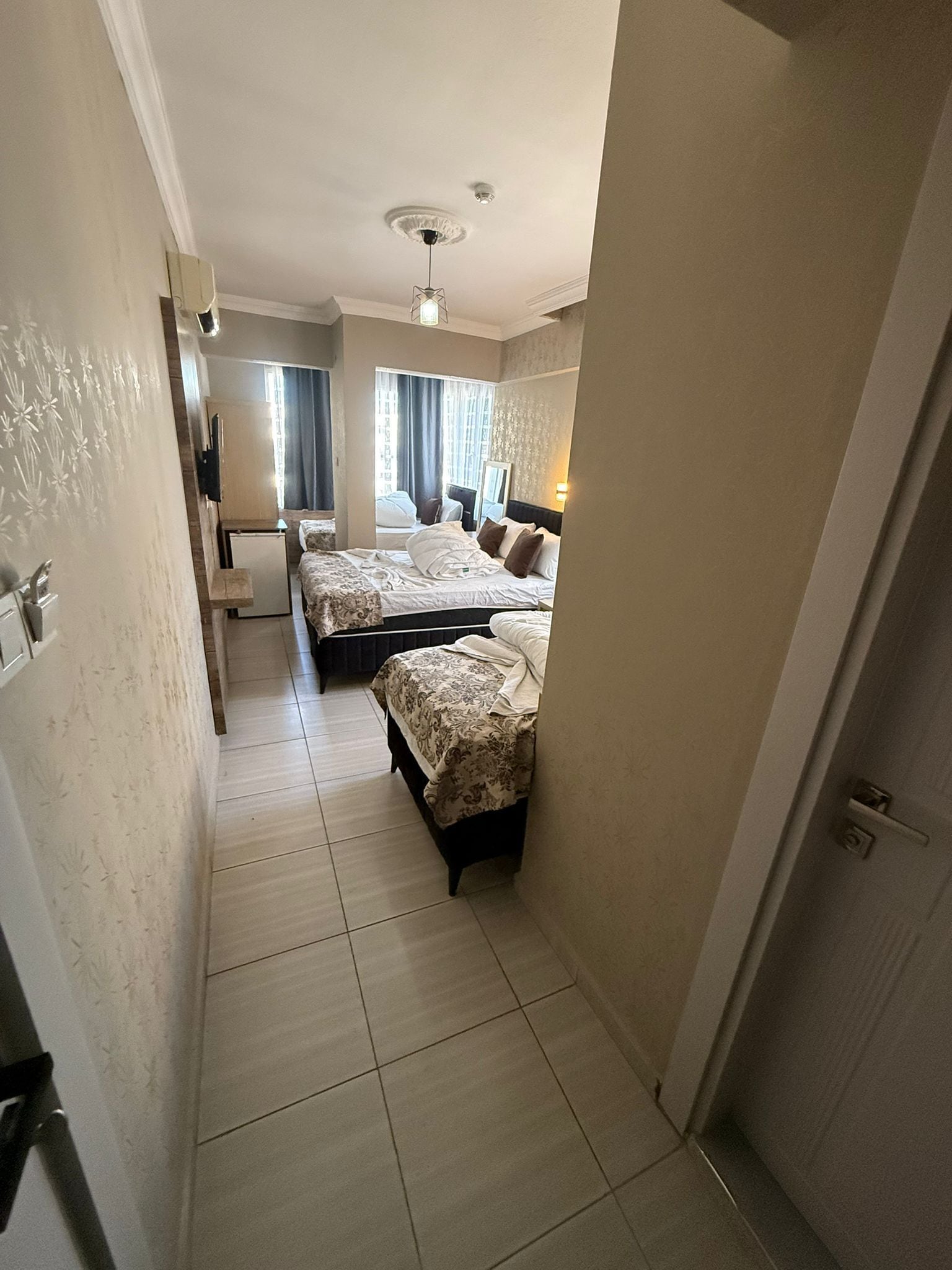 A narrow hallway leading to a bedroom with two beds, a small desk, and a mirror.