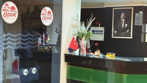 A hotel reception area with a glass door, a reception desk, a framed picture on the wall, and a signboard. - Özgür Family Otel (Antalya)