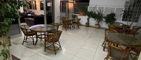 Un patio con mobiliario de mimbre, plantas en macetas y vista al interior.