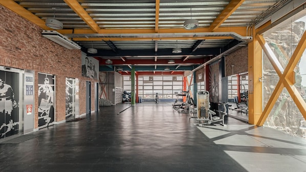 A spacious gym with exercise equipment, large windows, and a brick wall.