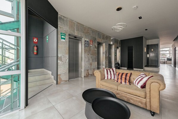 A modern lobby with a beige sofa, a staircase, and an elevator.