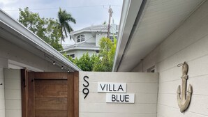 Eine Villa namens "Villa Blue" mit einer Holztür, einer Sitzgelegenheit im Freien mit Kissen und einer Wanddekoration in Form eines Ankers.