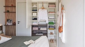 A bedroom with a bed, a wardrobe with hanging clothes, shelves with folded clothes, and a bedside table with a book and glasses. - ZEcamping 4* animé espace aquatique sauna hammam locatif TV LV BBQ (Aubigny-Les Clouzeaux)