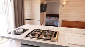 A modern kitchen with a gas stove, a small sink, and a countertop with a kettle. - ZEcamping 3* 200m plage locatif TV LV clim 40m2 6 pers (Hyères)