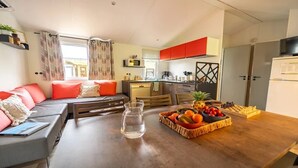 Ein gemütlicher Wohnbereich mit Sofa, Esstisch mit Obst, Küchenzeile und Fernseher.