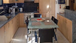 Moderni keittiö, jossa on lasinen ruokapöytä, puukaapit ja sisäänrakennettu uuni.