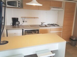 Eine kompakte Küche mit Mikrowelle, Kaffeemaschine, Spüle, Herd und kleinem Backofen.