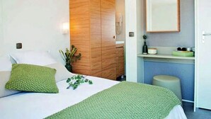 A bedroom with a bed, a wooden wardrobe, a mirror, and a small plant. - Camping 4 étoiles - Parc aquatique - ccbahgb (Saint-Cyprien)