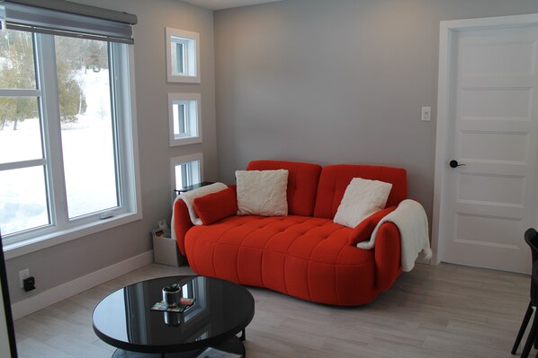 A room with a red sofa, a small round table, and a white door. - La Casa TiMoris (Wentworth-Nord)