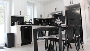 Una cocina moderna con armarios blancos, un refrigerador negro y un comedor con sillas negras.