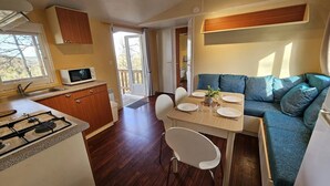Eine kompakte Küche mit Mikrowelle, Herd und Spüle, ein Essbereich mit Tisch und Stühlen sowie ein Sofa mit Kissen.