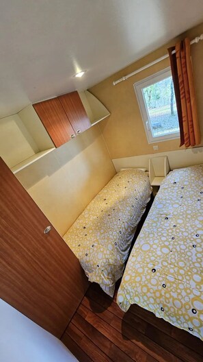 Een compacte kamer met twee bedden, een raam met gordijnen, een houten kast en een kleine tafel.