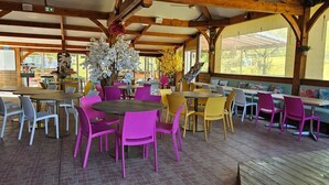 Ein Straßencafé mit runden Tischen und Stühhlen, Holzbalken und großen Fenstern.