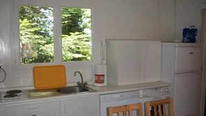 Uma cozinha compacta com fogão, pia e geladeira, uma mesa de jantar de madeira e uma janela com vista para vegetação.