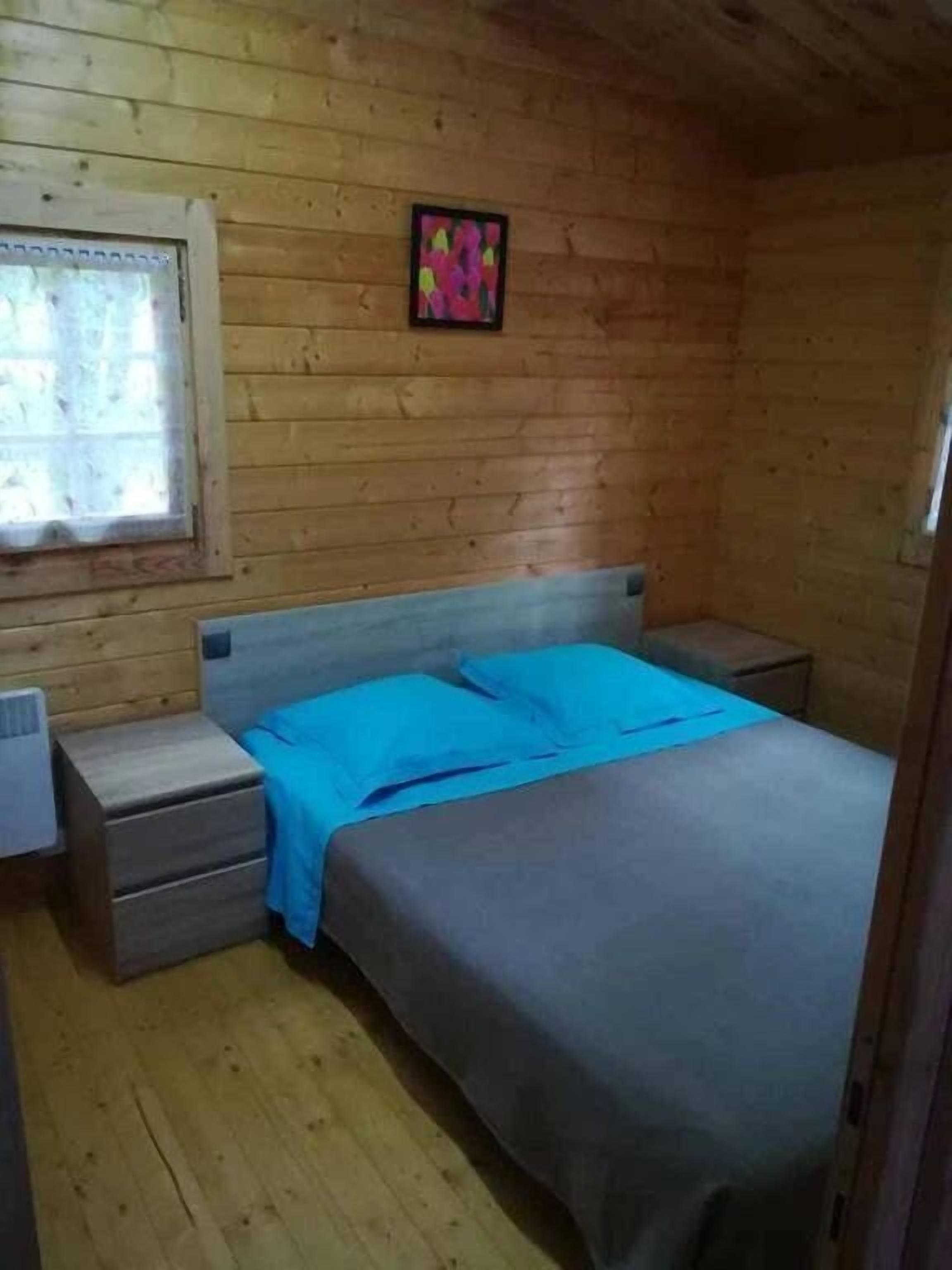 Een knus kamertje met houten wanden en een enkel bed met een blauwe deken.