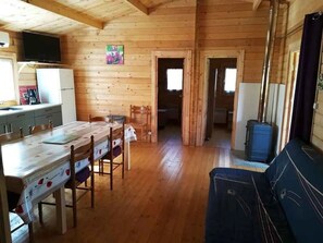 A wooden cabin interior with a dining area, kitchen, and a living space with a couch. - Chalet 3 étoiles - Piscine  - ccbfeag (Mayrac)