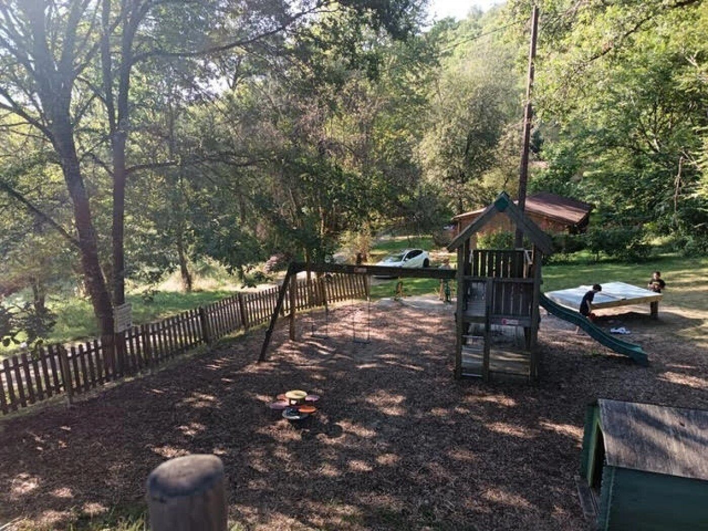 Une aire de jeux avec une clôture en bois, une petite structure en bois et un toboggan.