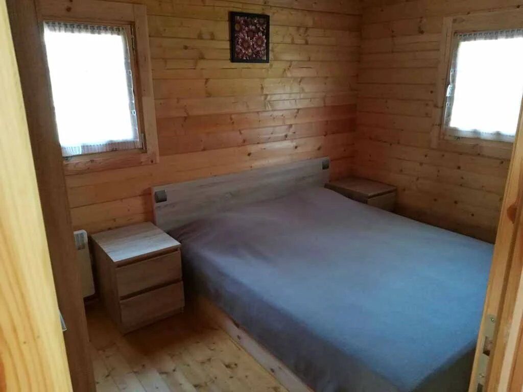 A small, wooden room with a bed, two nightstands, and a window.
