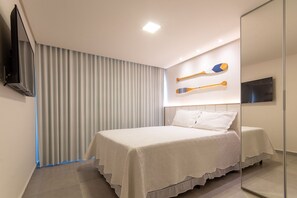 A modern bedroom with a large bed, a television, and two paddleboards on the wall. - Villa Del Porto #307 - Flat in Porto by Carpediem (Ipojuca)