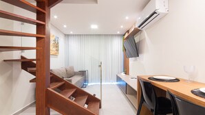 A modern apartment with a wooden staircase, a dining area with a wooden table and chairs, a kitchen area, and a living room with a sofa and a TV. - Villa Del Porto #307 - Flat in Porto by Carpediem (Ipojuca)