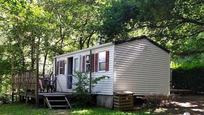 Une petite maison mobile d’un seul étage, dotée d’une véranda et entourée d’arbres.