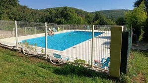 A rectangular swimming pool with a metal fence, surrounded by grass and trees.