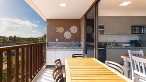 Varanda com mesa e cadeiras de madeira, cozinha com bancadas de granito e decoração na parede.