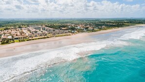 Vista aérea de um resort à beira-mar, com vários edifícios, uma praia de areia e águas azul-turquesa.