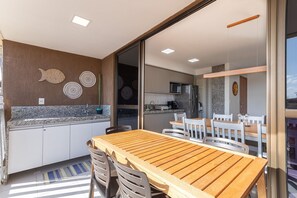 A modern kitchen with white cabinets, a wooden dining table, and a view of the dining area. - Cupe Beach Living #102d - Triple by Carpediem (Ipojuca)