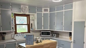 A compact kitchen with grey cabinets, a wooden countertop, a microwave, and a sink. There are two red stools and a window with a view of greenery. - Pet-Friendly Home in Downtown Balaton (Balaton)
