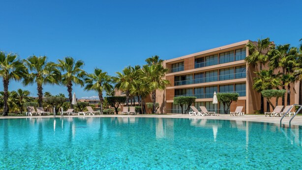 A swimming pool with lounge chairs and palm trees, surrounded by a modern building. - Salgados Resort Beach & Nature Escape (Albufeira)