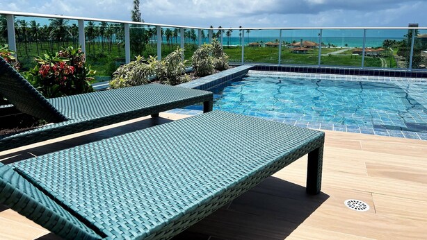 A poolside area with lounge chairs and a view of the ocean. - Cupe Garden #315 - Porto de Galinhas by Carpediem (Ipojuca)