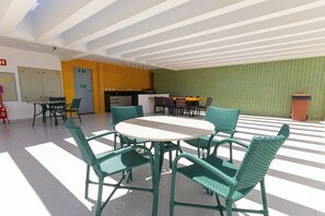 A spacious indoor area with a round table and chairs, a kitchen area, and a green-tiled wall. - Cupe Garden #315 - Porto de Galinhas by Carpediem (Ipojuca)