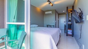 A hotel room with a bed, a chair, a TV mounted on the wall, and an air conditioning unit. - Cupe Garden #315 - Porto de Galinhas by Carpediem (Ipojuca)