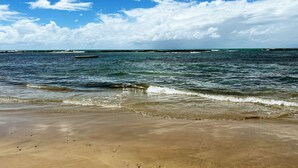 A beach with clear blue water, a sandy shore, and a distant rocky outcrop. - Cupe Garden #315 - Porto de Galinhas by Carpediem (Ipojuca)