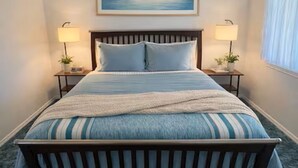 Un dormitorio con cama de madera, dos lámparas de noche, un cuadro enmarcado en la pared y una ventana con cortinas.