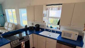 Cocina compacta con estufa, horno, pileta y microondas. Incluye alacenas y un ventanal con cortinas.
