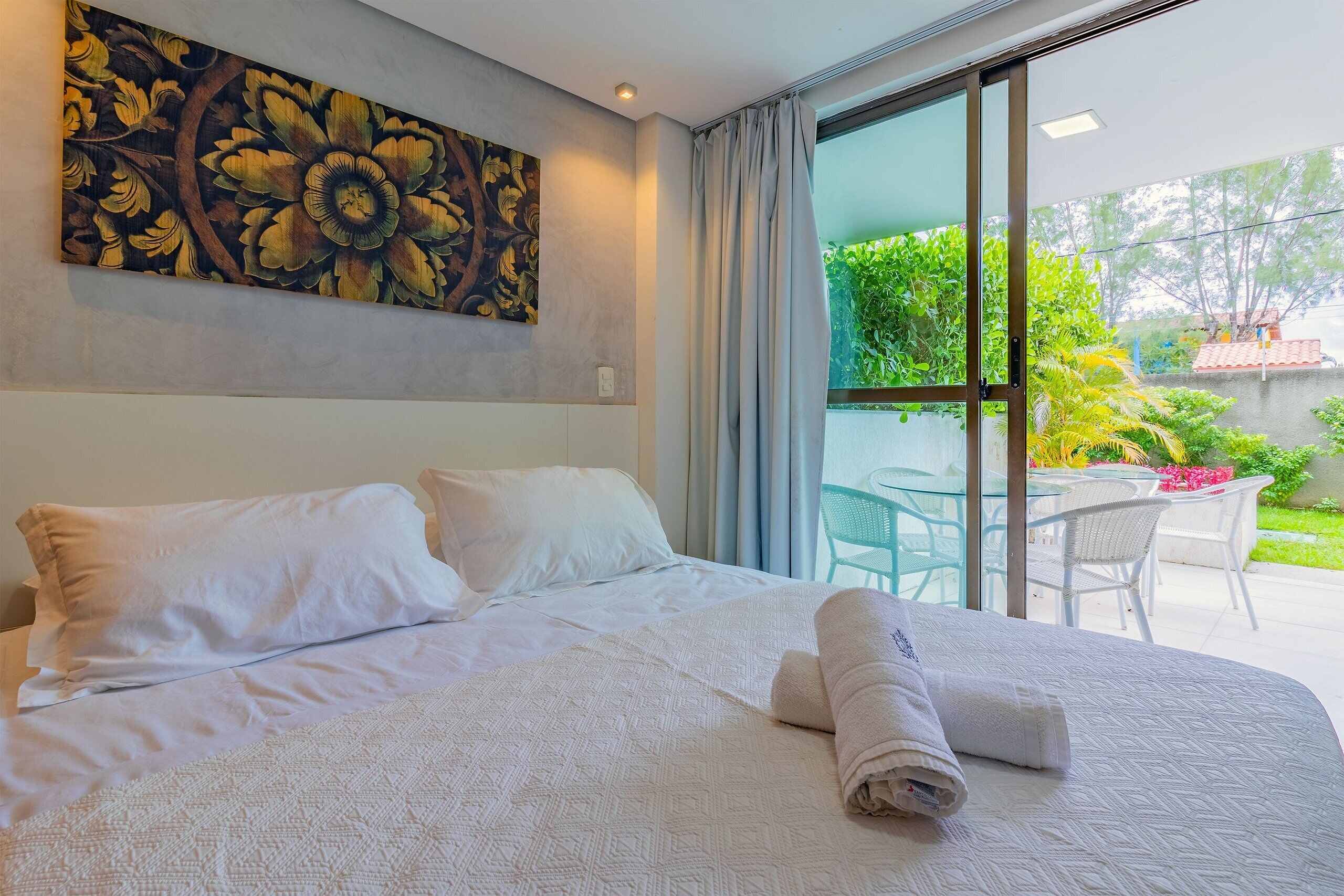 Habitación de hotel con una cama grande, un cuadro en la pared y vistas al jardín a través de la ventana.