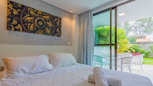 Habitación de hotel con una cama grande, un cuadro en la pared y vistas al jardín a través de la ventana.