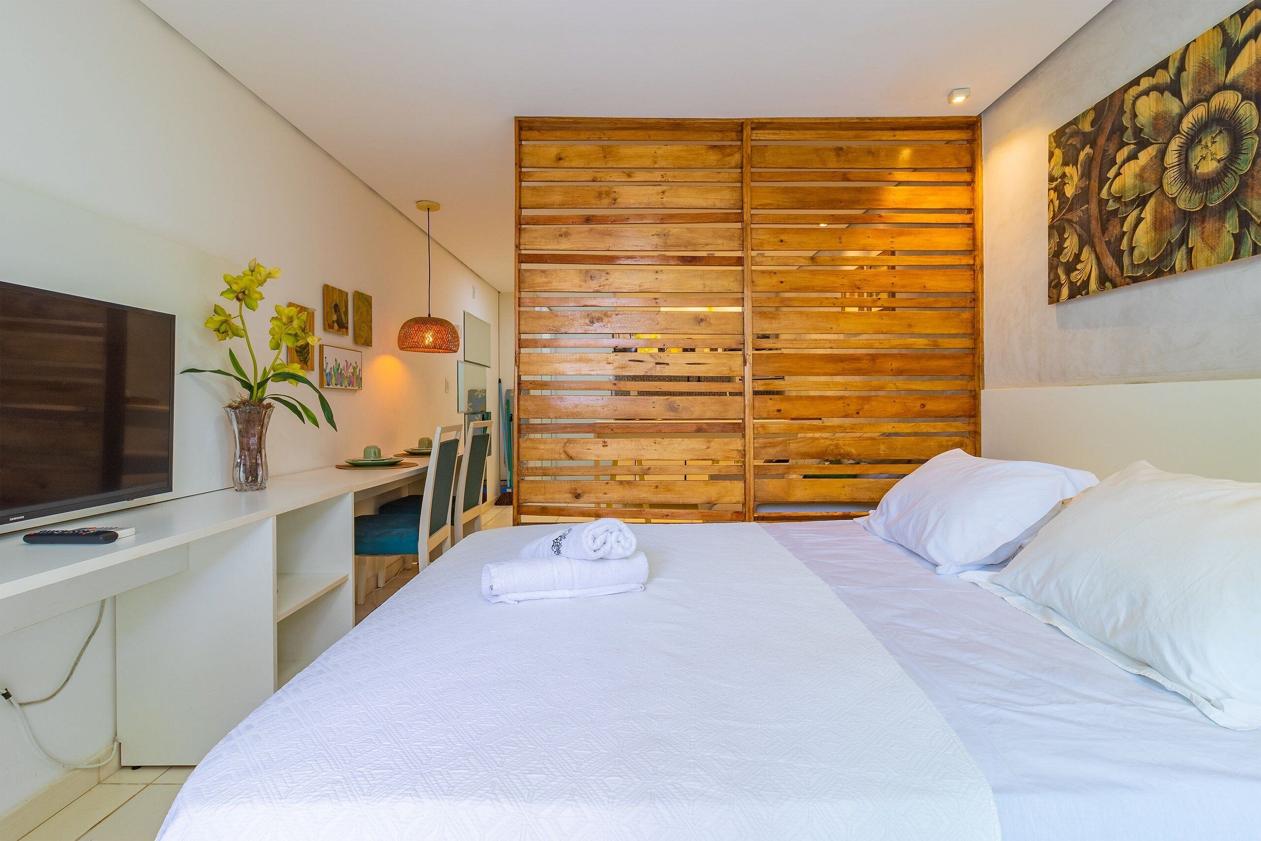 Quarto de hotel moderno com uma cama grande, televisão de tela plana, escrivaninha e um painel de madeira.