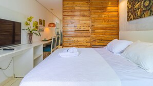 Una habitación de hotel moderna con una cama grande, un televisor de pantalla plana, un escritorio y un separador de madera.